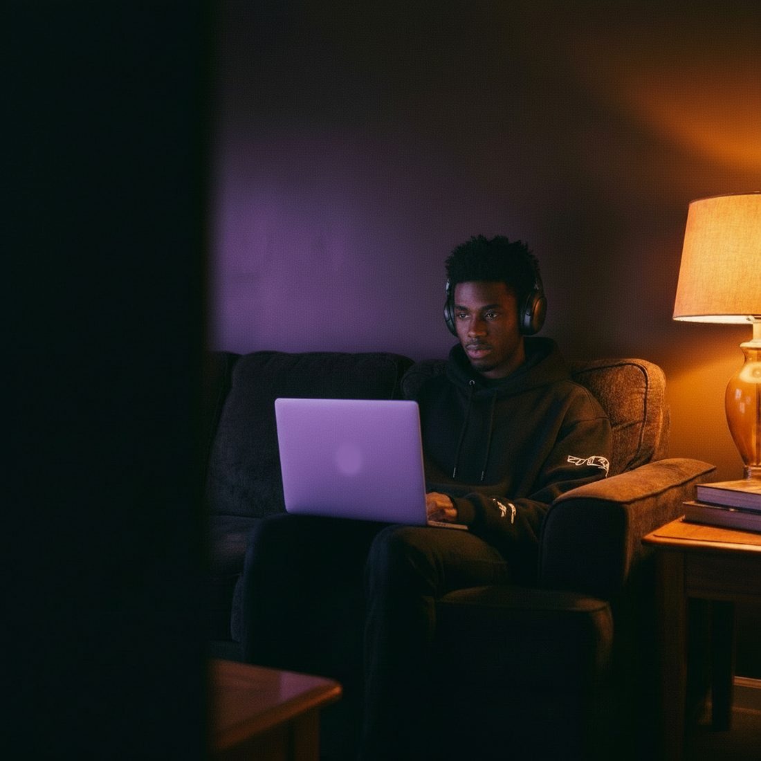 A man in headphones with a laptop in the evening: warm lamp light and the violet glow of the screen